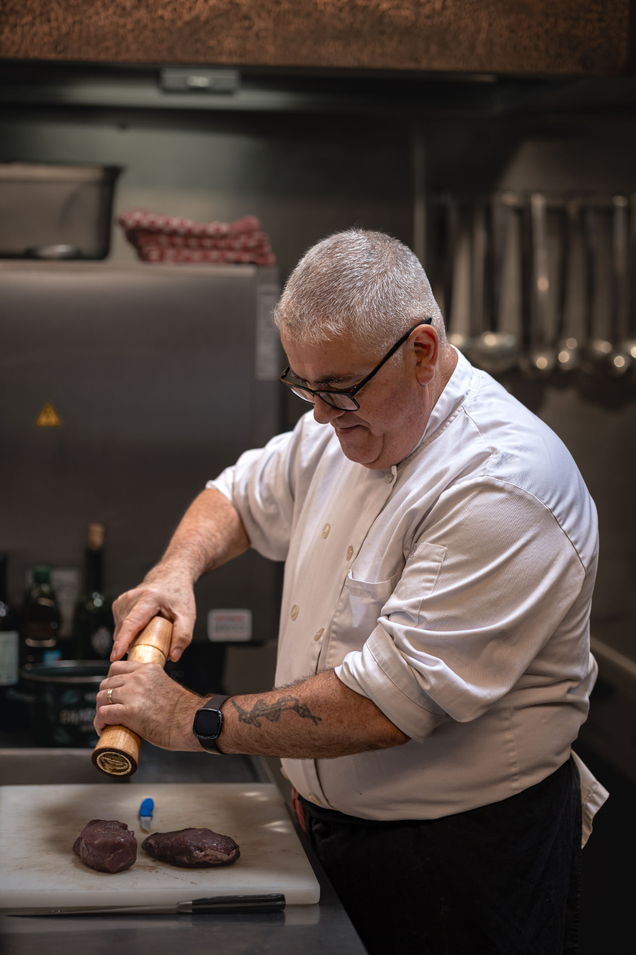Le chef de La Roue d'Or en cuisine, assaisonnant deux pièces de viande au moulin à poivre