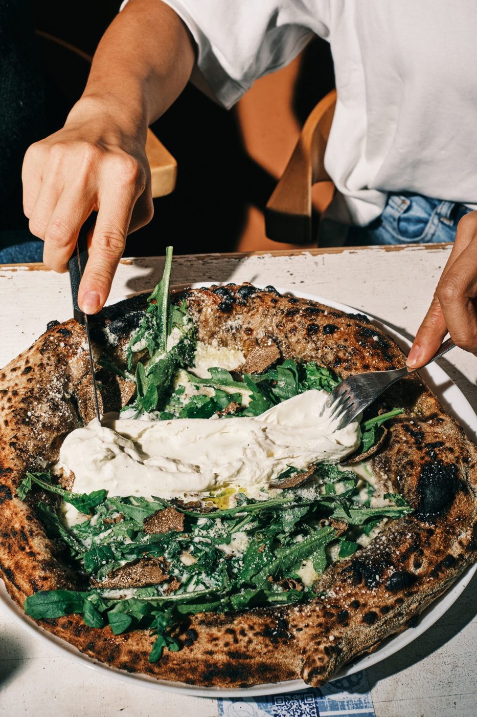 Pizza aux légumes verts et stracciatella découpée sur la table chez Biga