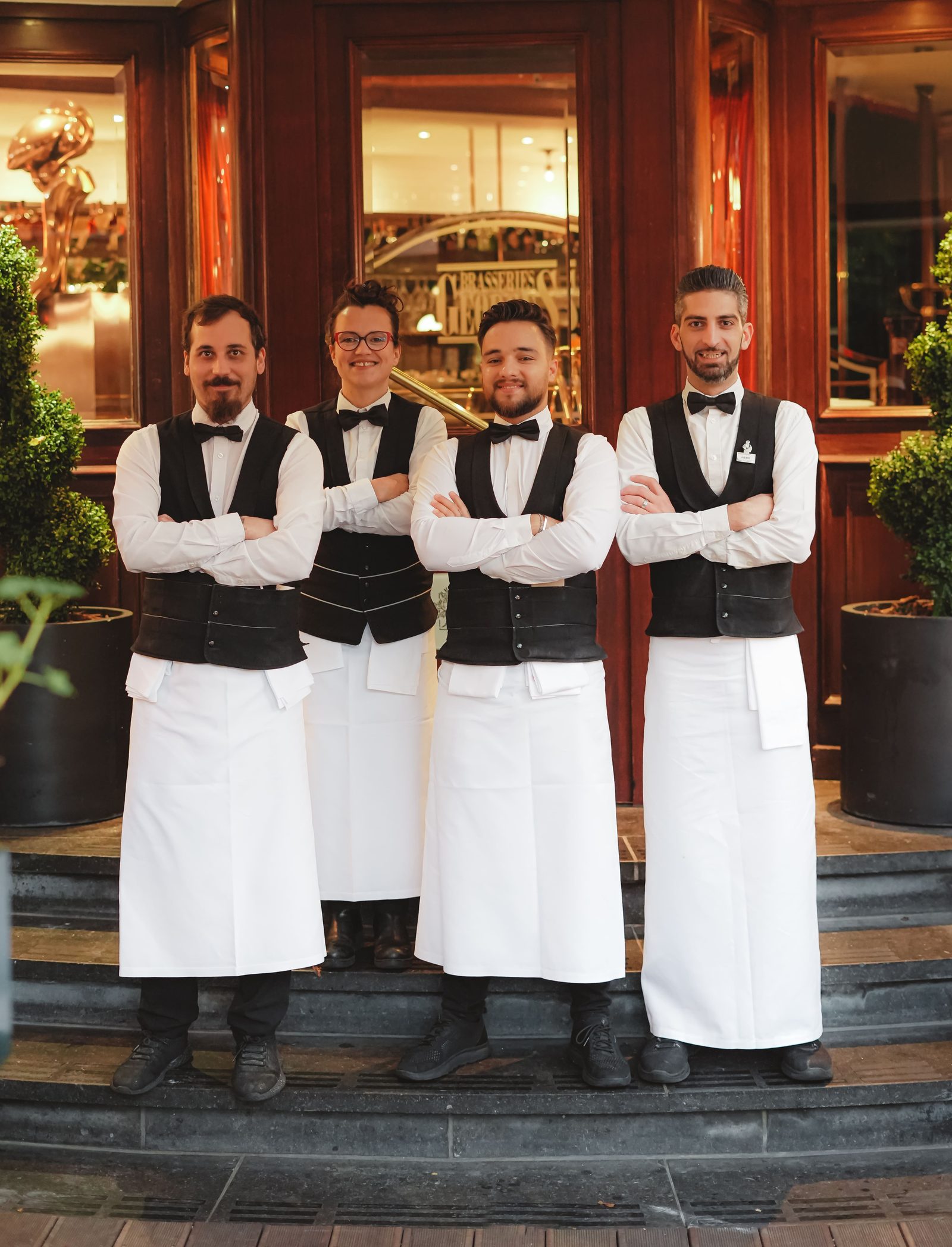 Quatre serveurs des Brasseries Georges en gilet et tablier blanc