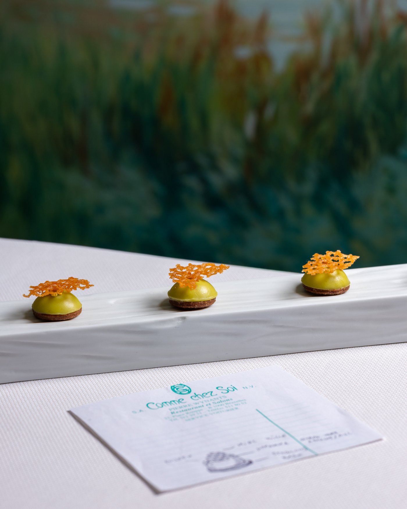 Mignardises et addition posées sur la nappe du Comme chez Soi