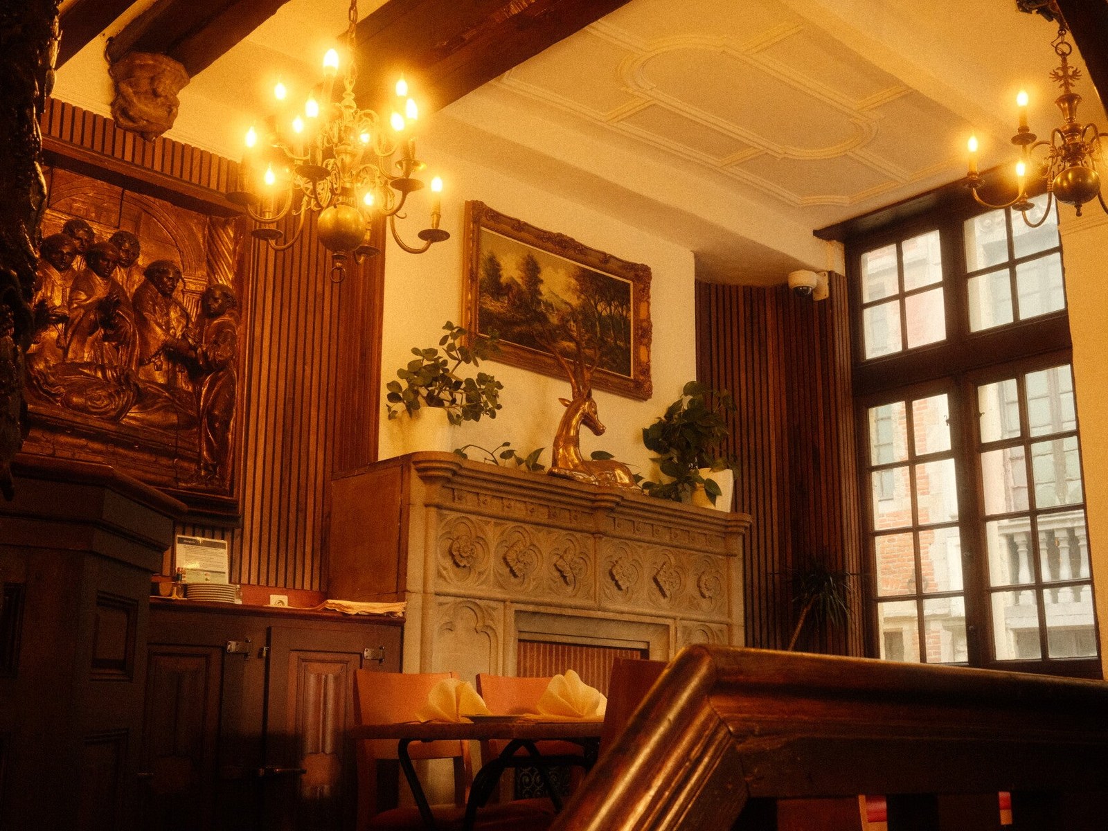 Intérieur de la Brasserie Le Cerf : boiseries sculptées, cheminée de pierre et lustres à bougies