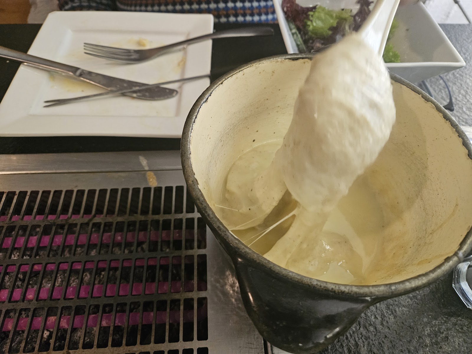 Caquelon de fondue savoyarde filante servi sur la table à grill intégré