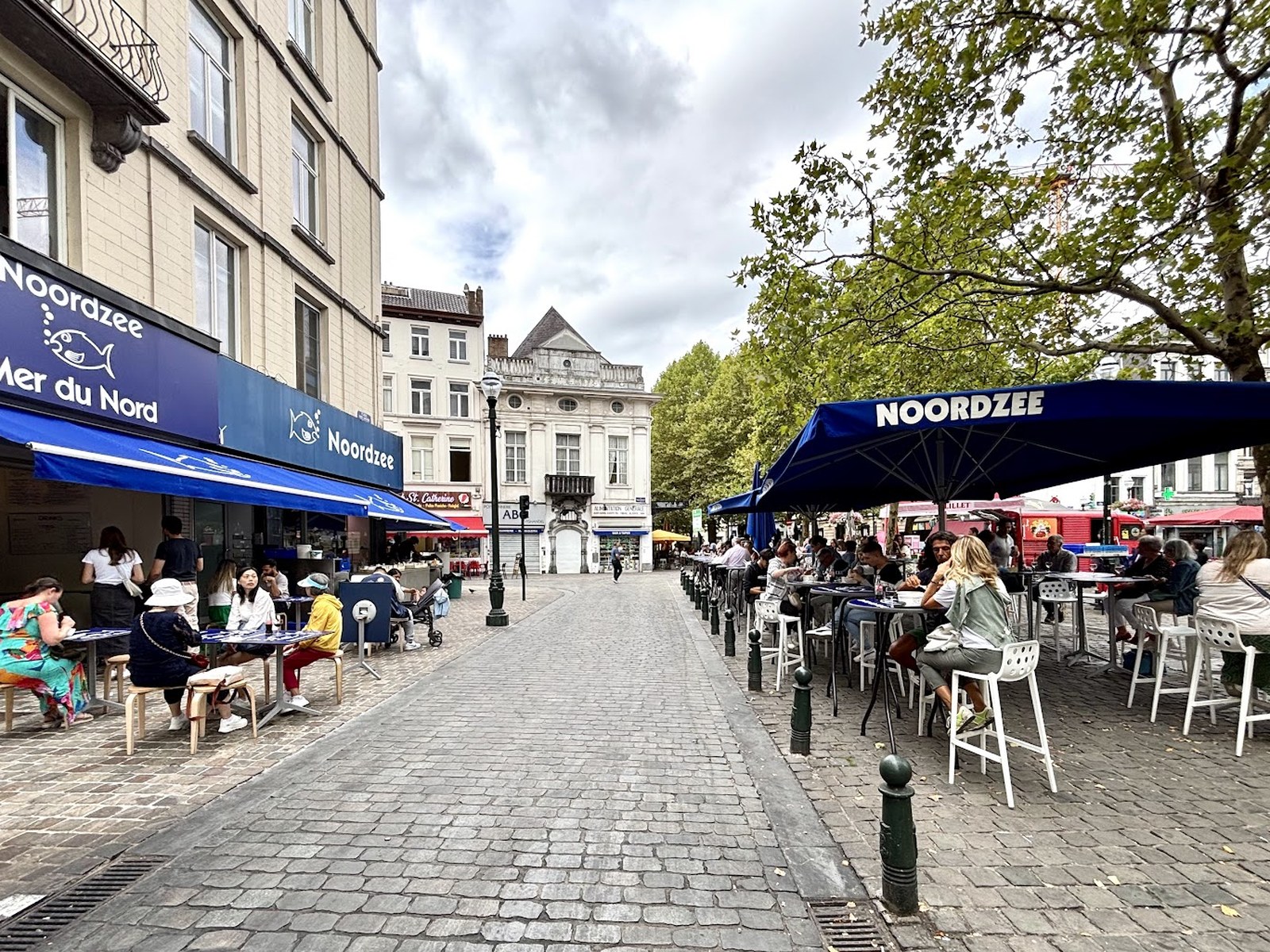 Terrasse animée de la Mer du Nord sur la place Sainte-Catherine, tables hautes et parasols bleus