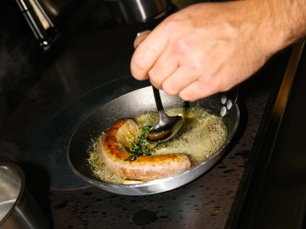 Saucisse arrosée au beurre dans une poêle en cuisine chez Moutarde