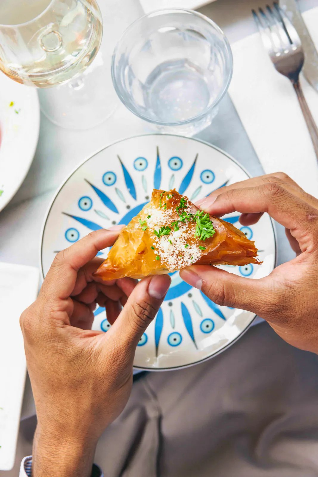Feuilleté grec tiropitakia partagé à deux mains au-dessus d'une assiette peinte